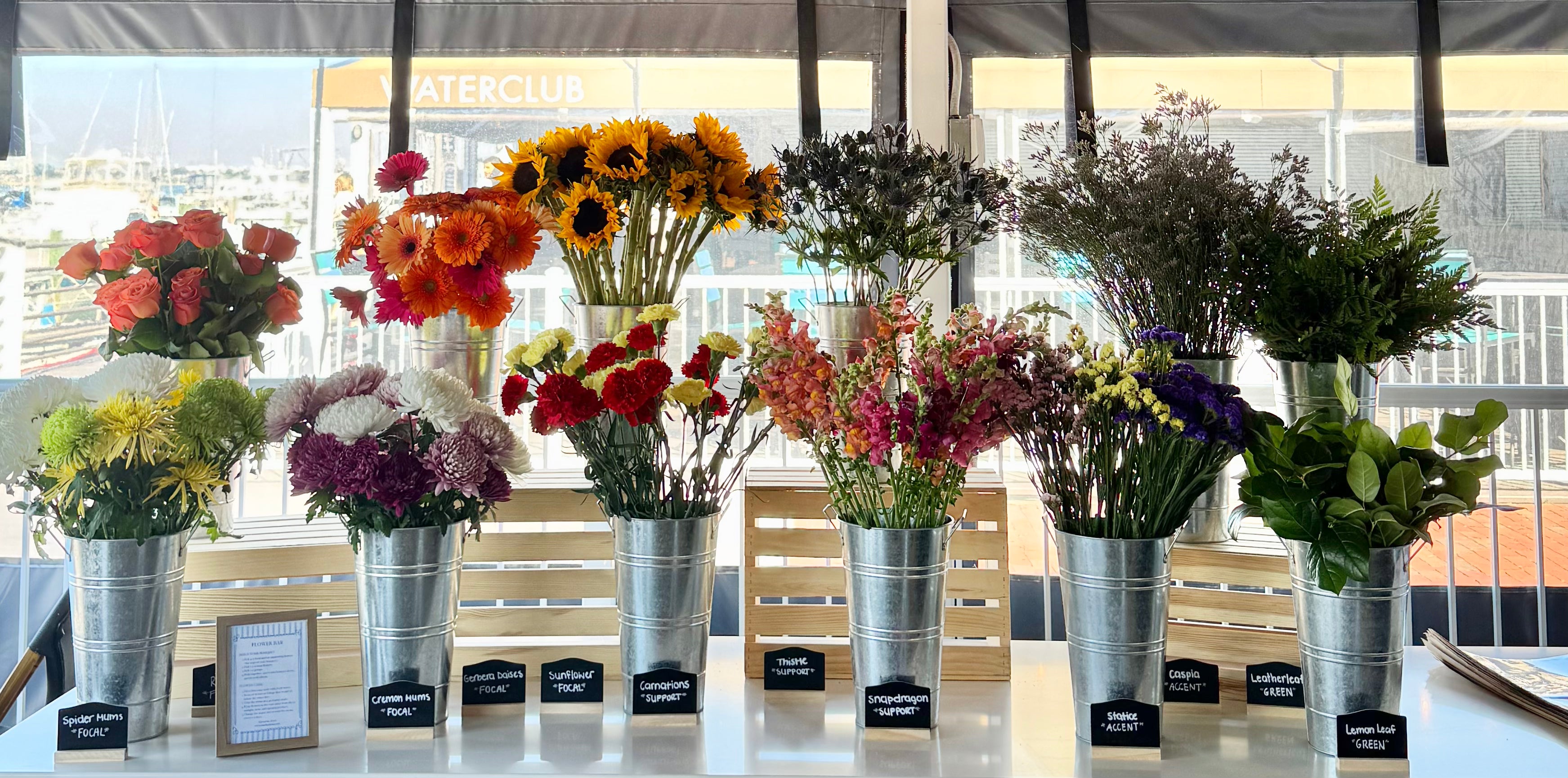 DIY flower bouquet bar for bridal shower, baby shower, party, or event. Different types of colorful flowers in metal buckets.