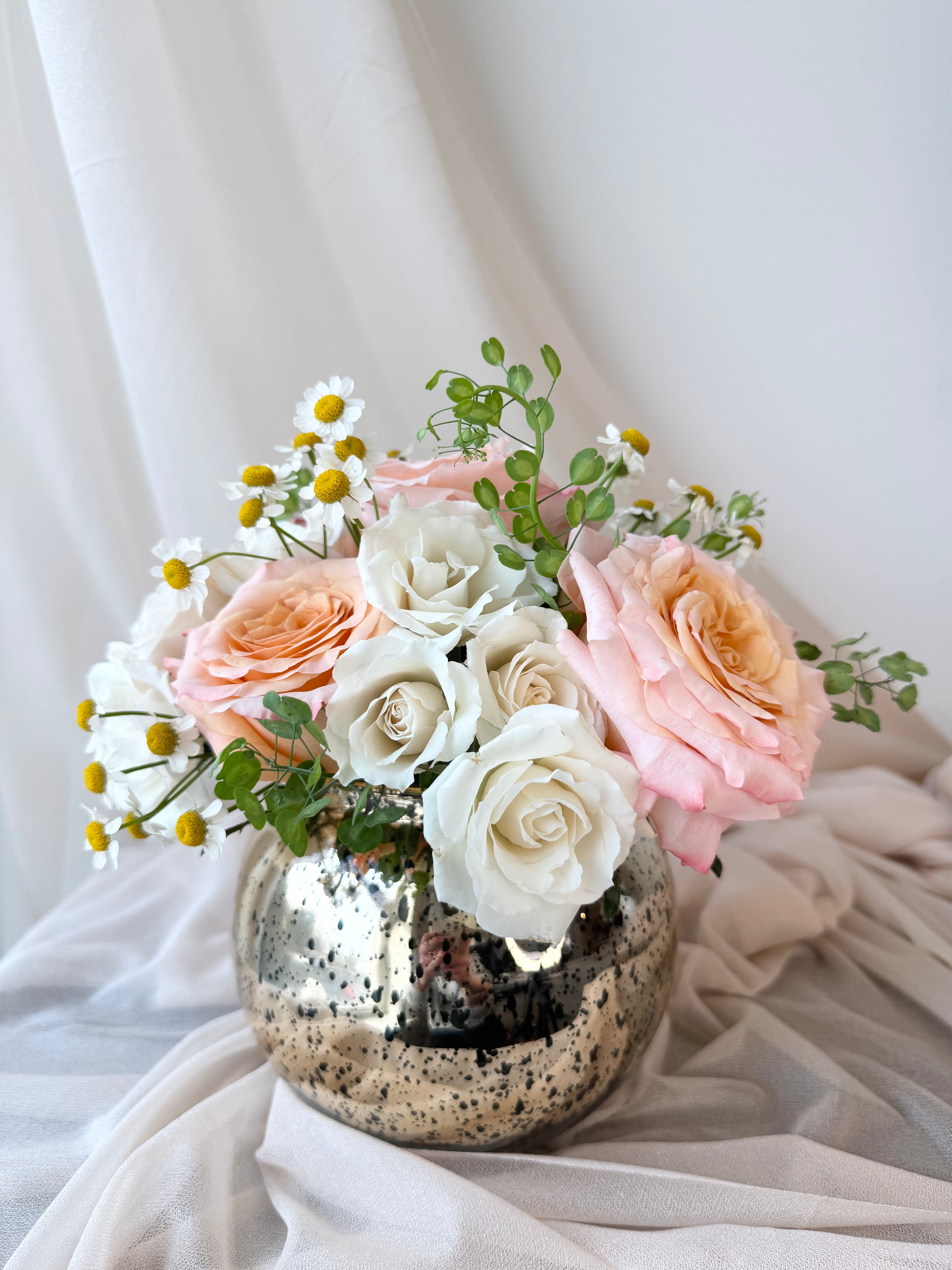 Flower arrangement of pink and white roses in a decorative vase on a light fabric background