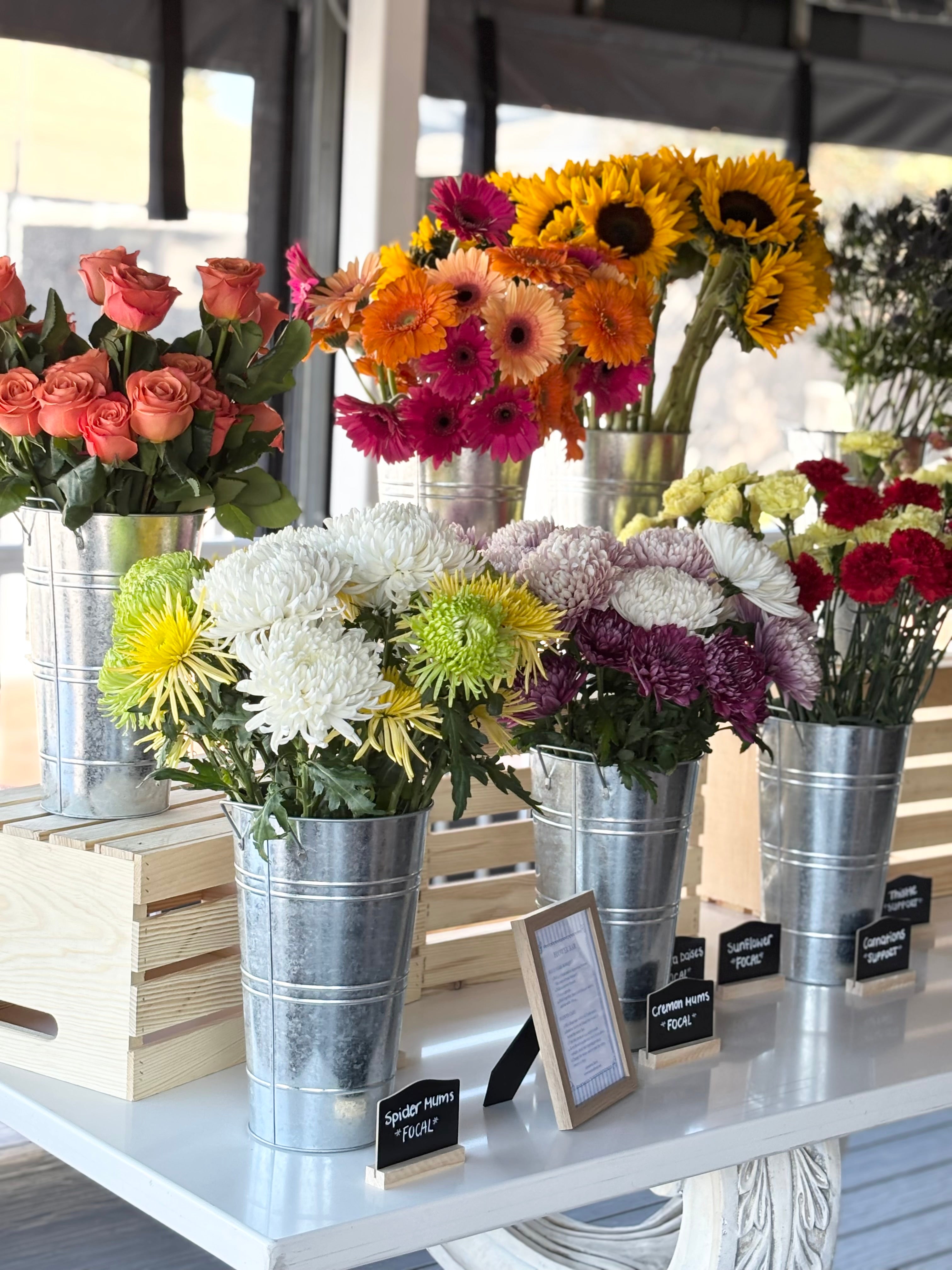 Assorted flowers in metal buckets on a table for flower bouquet bar at a bridal shower, baby shower, party, or event